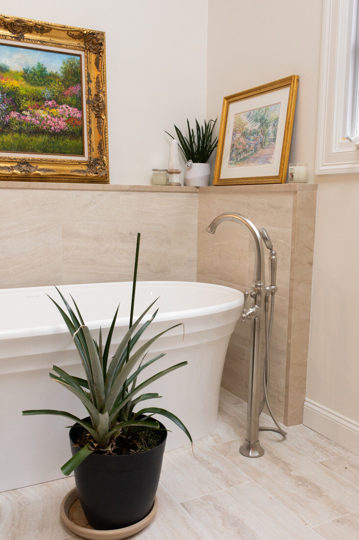 Elegant freestanding tub in a Westwood, MA bathroom remodel by Tom Curren, featuring neutral stone tile and framed artwork