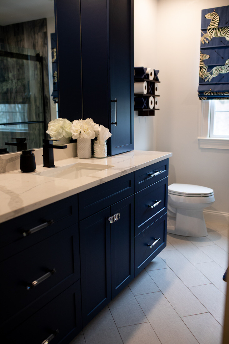 Elegant navy blue vanity in a Needham, MA bathroom remodel by Tom Curren, featuring new tile floor and new stone countertops