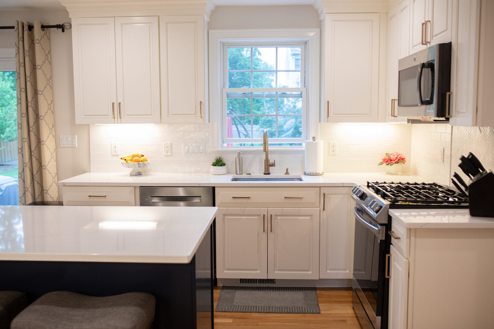 White kitchen with a stylish farmhouse sink, bright countertops, and modern appliances, part of a renovation by Tom Curren Companies in Metrowest Boston