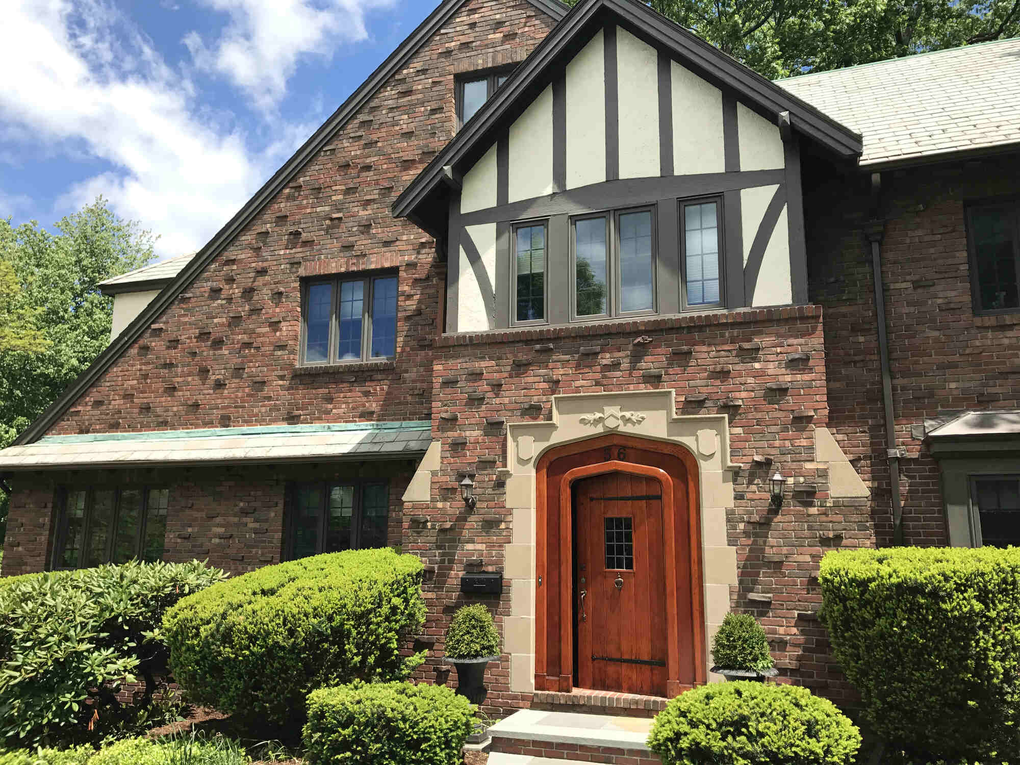 Tudor-style brick home with a newly stained wooden front door, part of a restoration by Tom Curren in Newton, MA