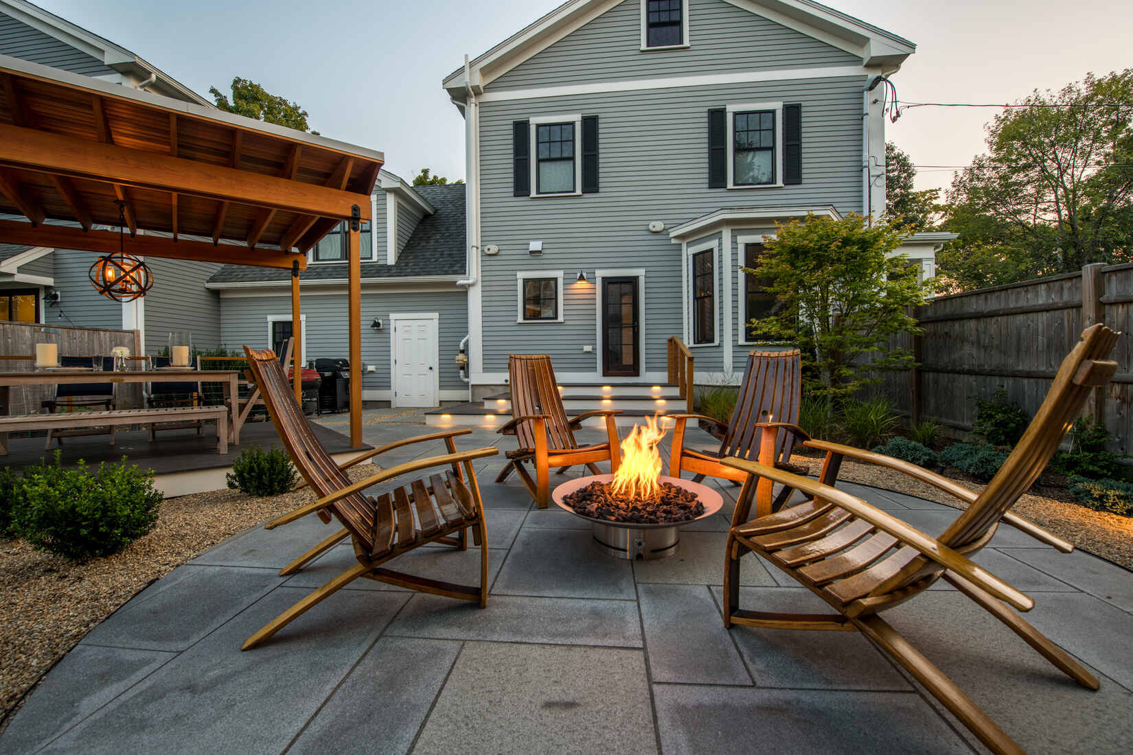 Cozy fire pit area on a stone patio with wooden Adirondack chairs, part of a backyard remodel by Tom Curren in Auburndale, MA