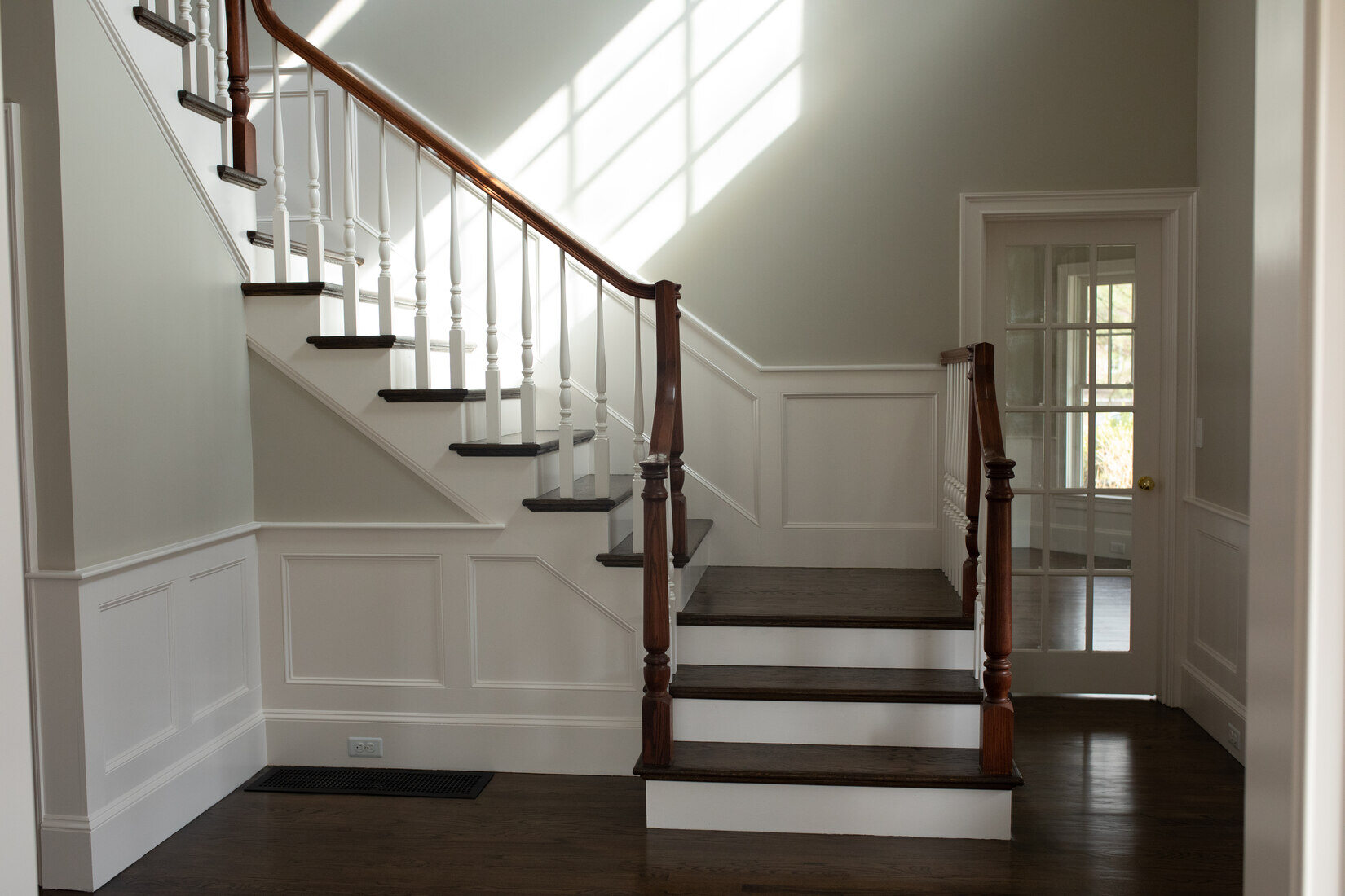 Grand staircase in Lincoln, MA, featuring fresh paint, white trim, and dark wood steps for a classic home entrance by Tom Curren