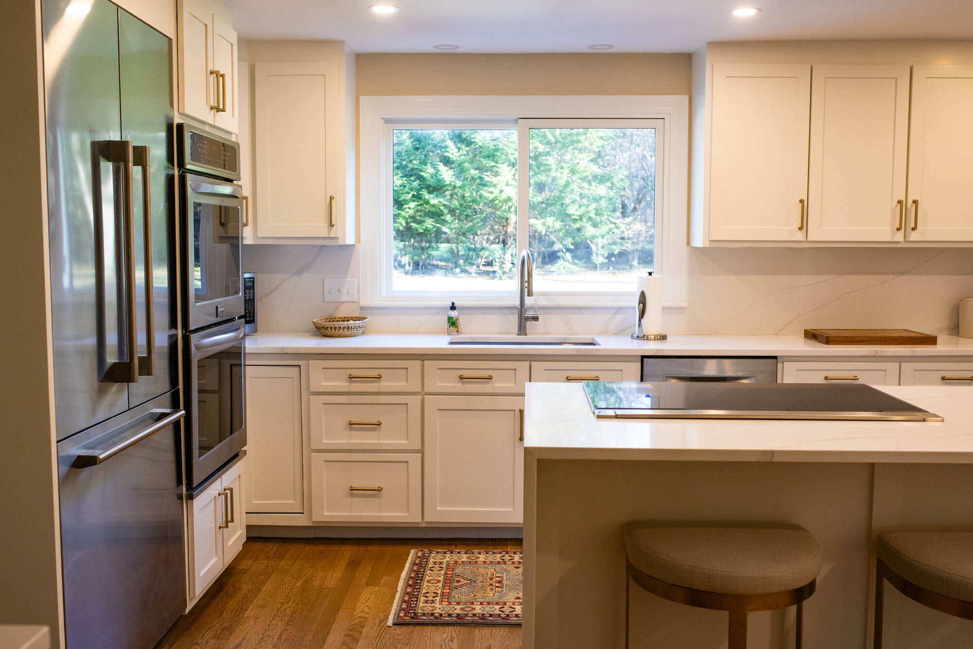 Bright and airy kitchen renovation in Sudbury, MA, by Tom Curren, featuring white cabinetry, a spacious island, and a window view