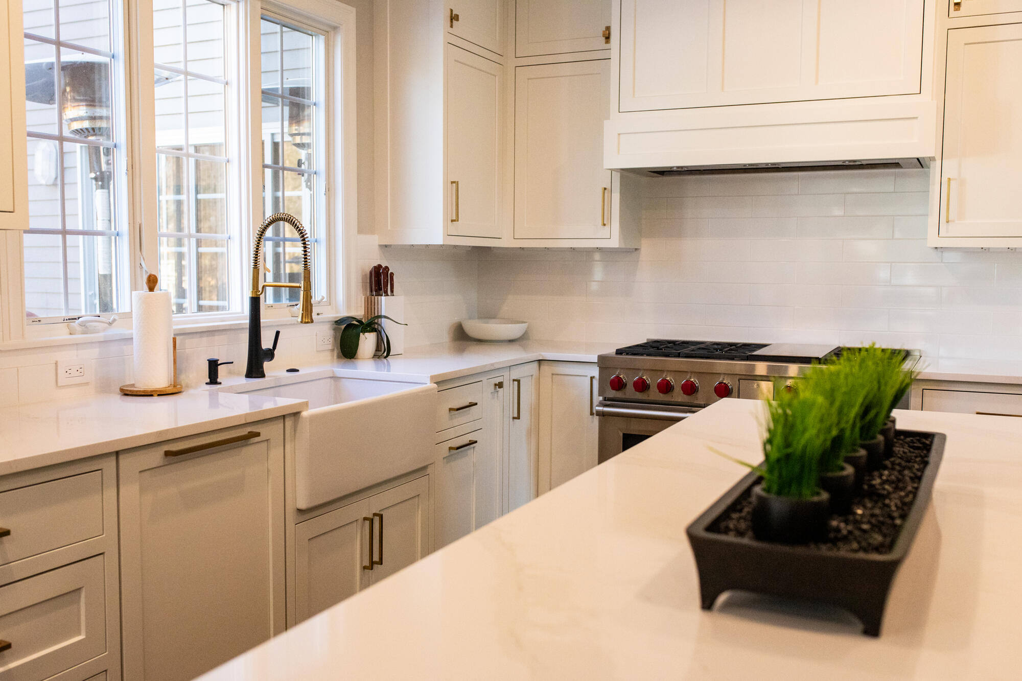 Bright and modern kitchen remodel in Bedford, MA by Tom Curren, featuring white shaker cabinets, new tile backsplash, brass hardware, and a spacious island
