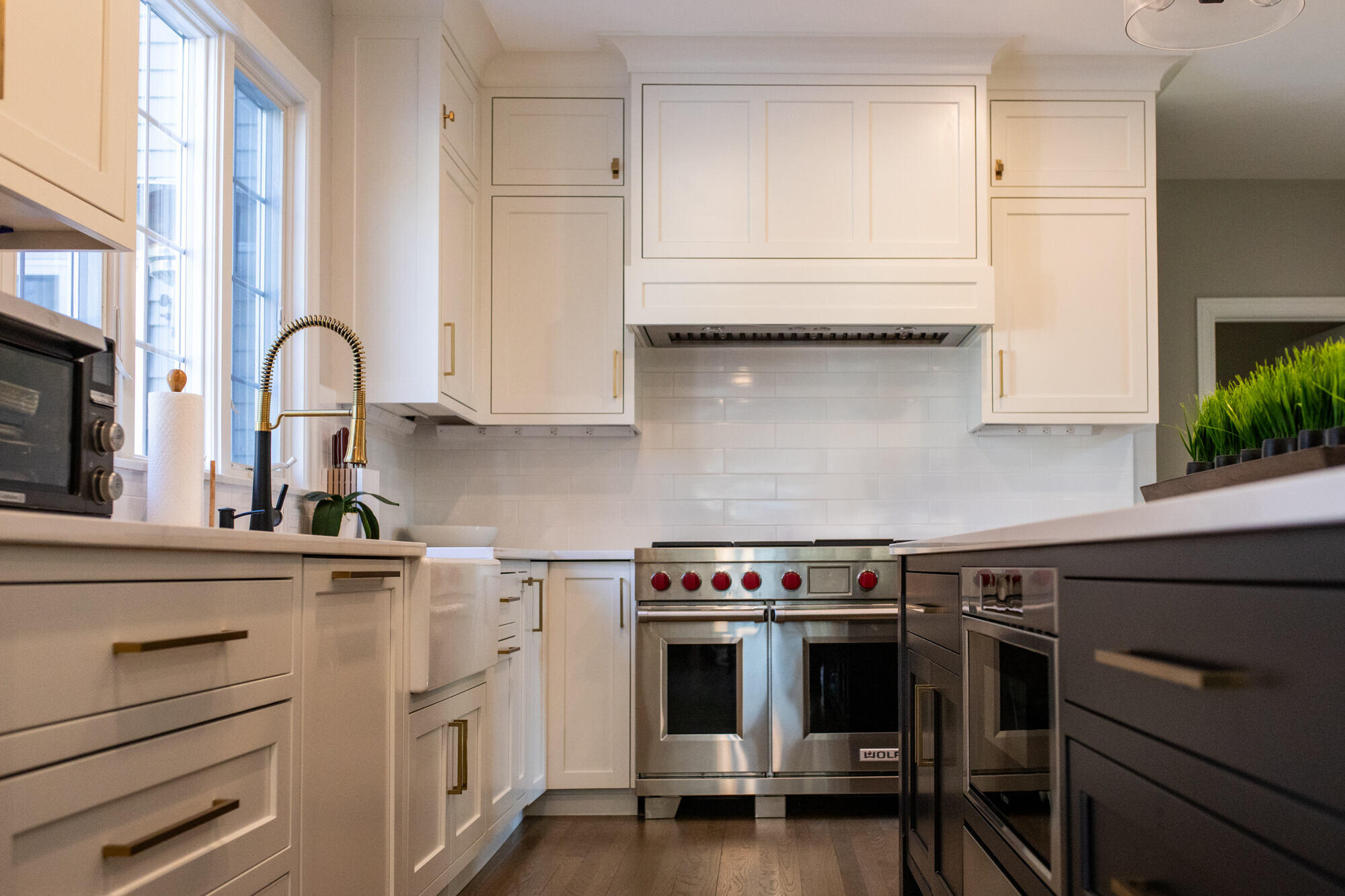 Elegant kitchen remodel in Bedford, MA by Tom Curren, highlighting a Wolf range, custom white cabinetry, blue island, and brass fixtures