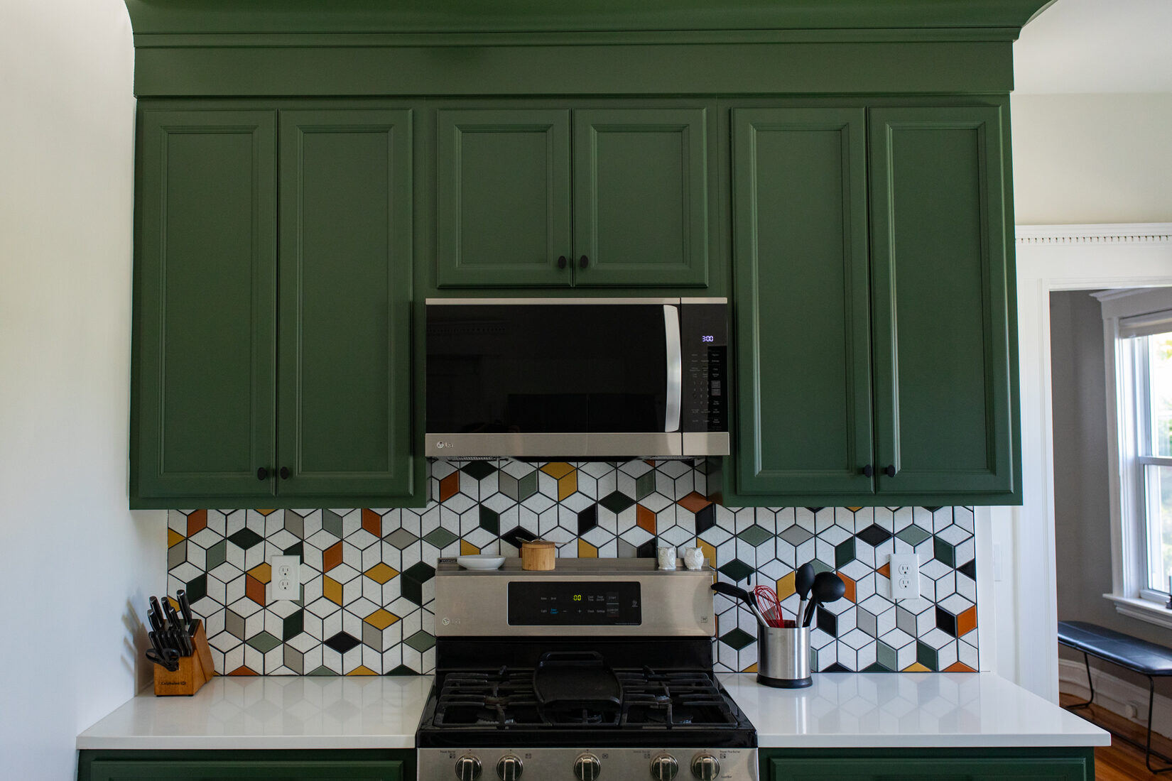 Close-up of a custom kitchen remodel in Somerville, MA, by Tom Curren, featuring dark green painted cabinetry and a geometric tile backsplash