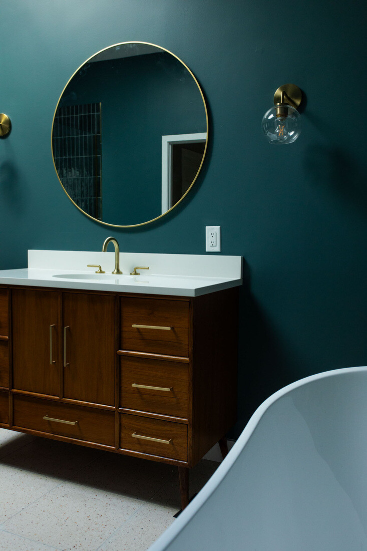 Modern bathroom renovation in Concord, MA, with sleek wood cabinetry, a round mirror, and brass fixtures
