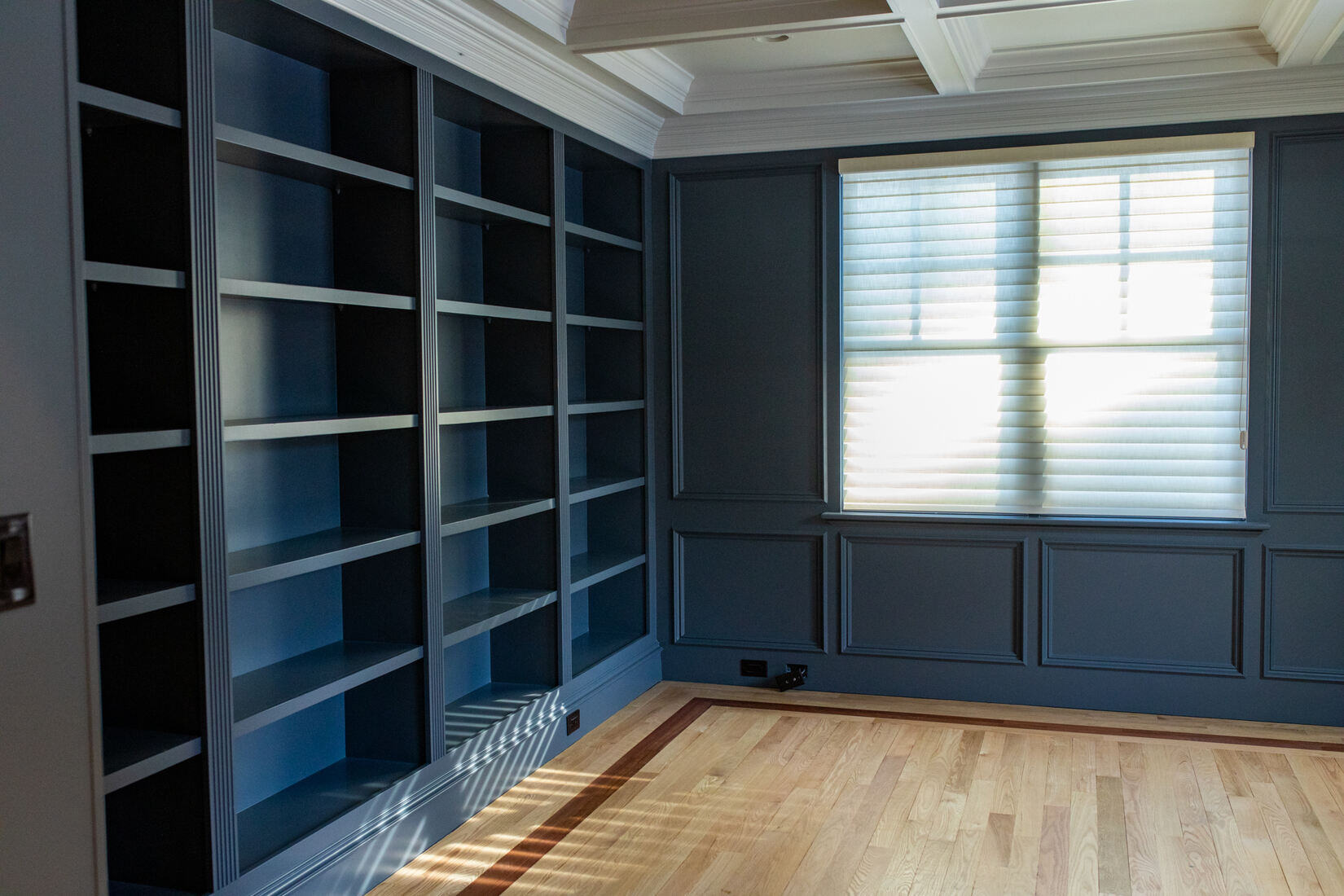 Custom-built dark blue bookshelves in a newly remodeled home office by Tom Curren Companies in West Metro Boston