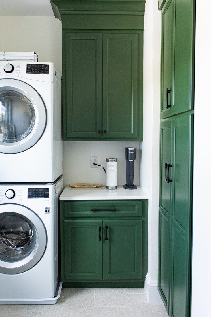 Stylish laundry room remodel featuring deep green cabinetry and a stacked washer-dryer setup by Tom Curren Companies in West Metro Boston