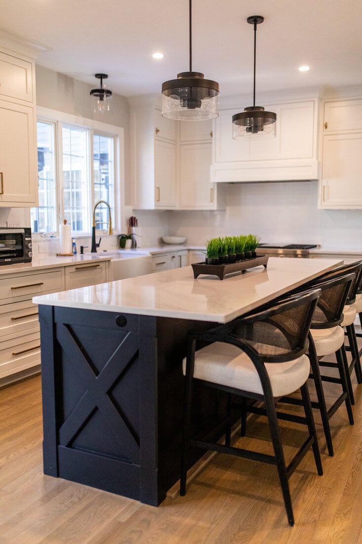 Modern kitchen remodel in Bedford, MA by Tom Curren, featuring a black island, white shaker cabinets, and pendant lighting