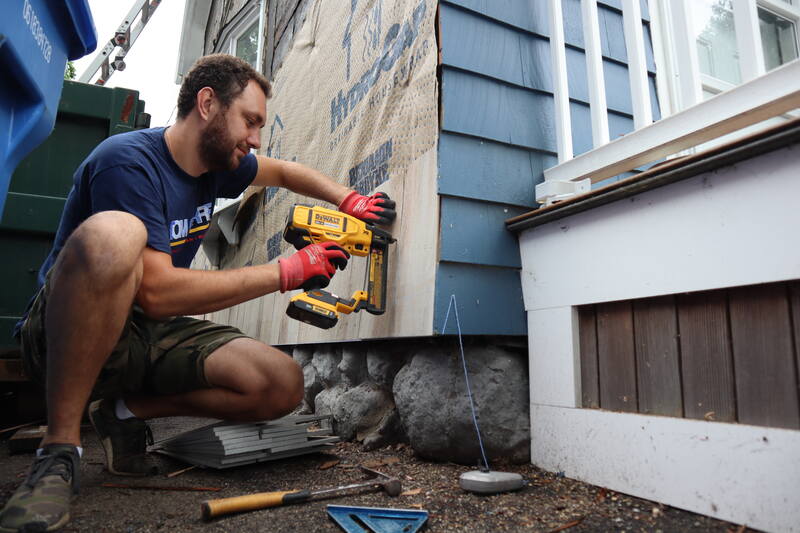 Tom Curren employee nailing siding on a house.